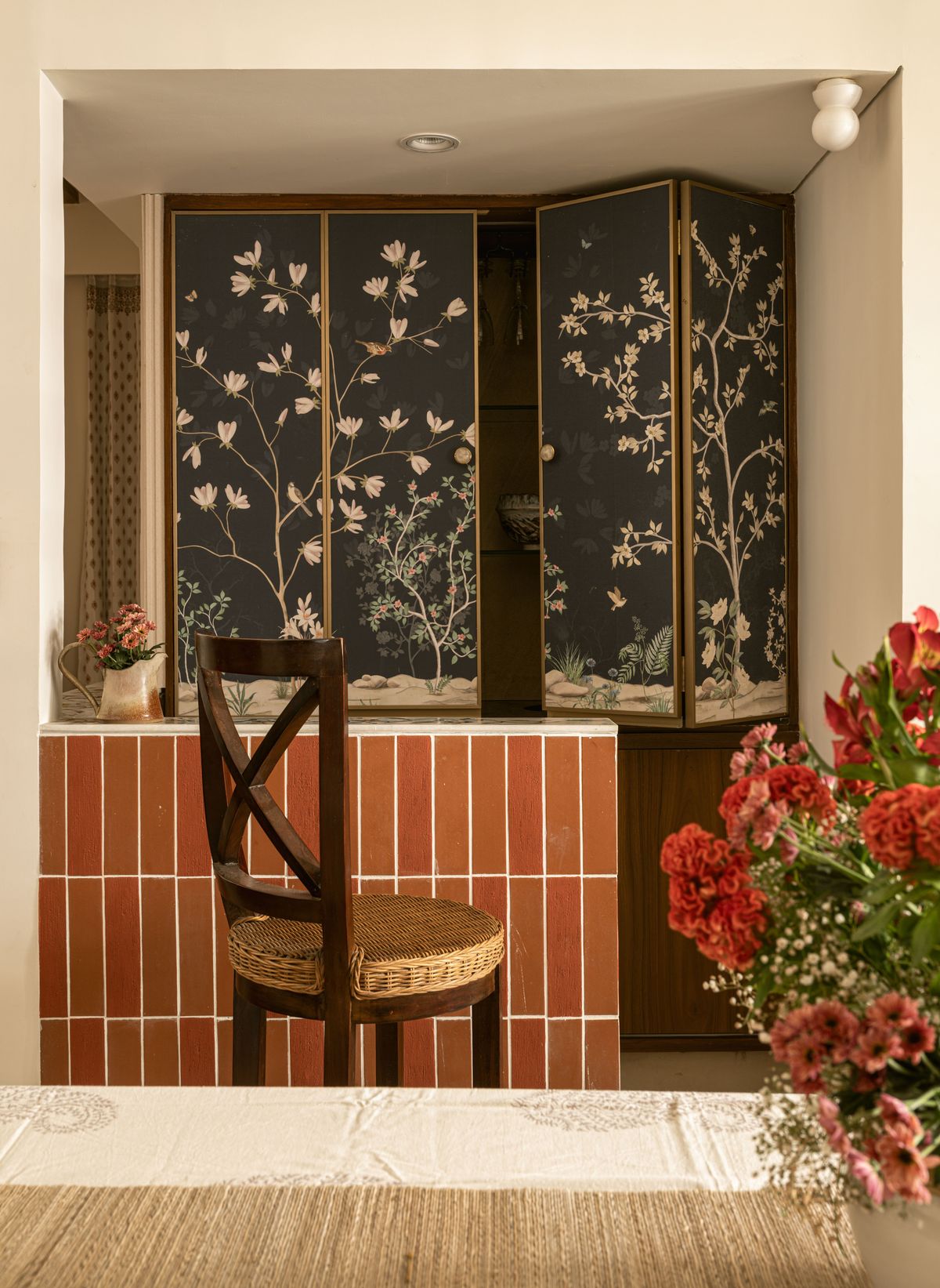 Bar unit with dark chinoiserie folding doors above terracotta tiles