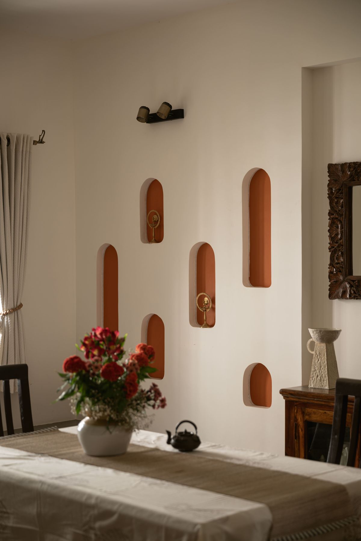 Arched terracotta niches holding brass artefacts beside the dining table